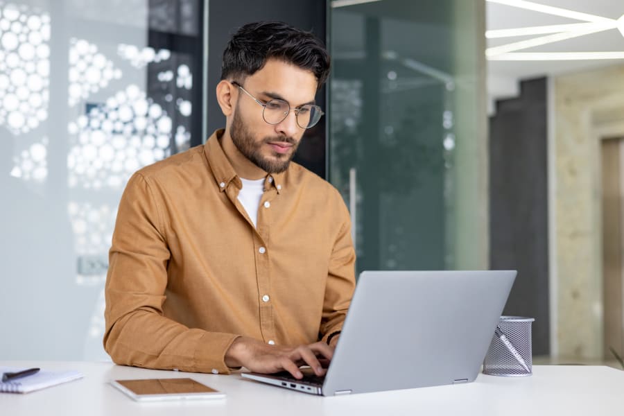 A young man in glasses working on a laptop in a stylish office setting