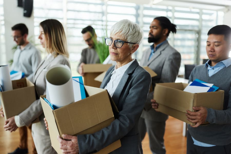 Large group of displeased business people carrying carton boxed with their belongings after being fired from their jobs.