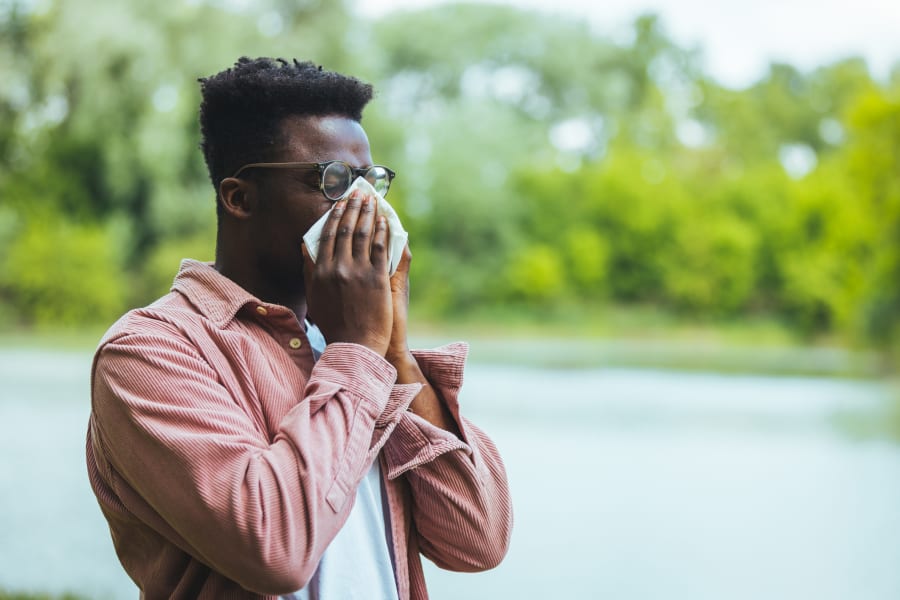 A Black man blowing his nose in a park