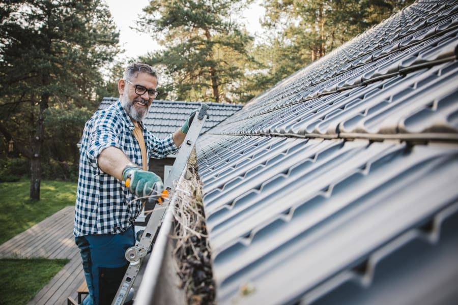 A man cleaning leaves from guttering of house