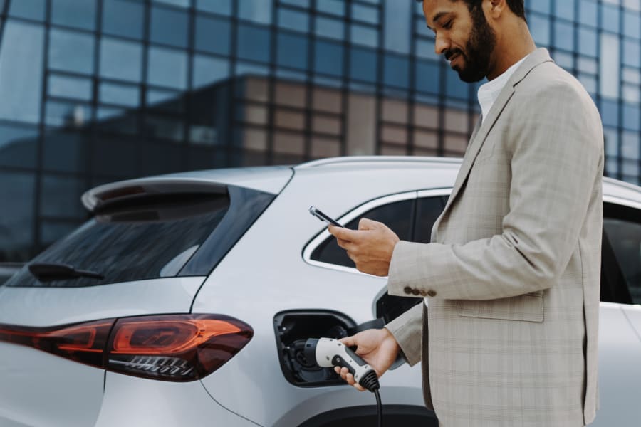 Man charging electric vehicle while looking at his phone