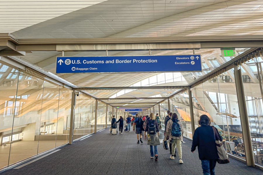 People in an airport walking under a U.S. Customs and Border Protection sign