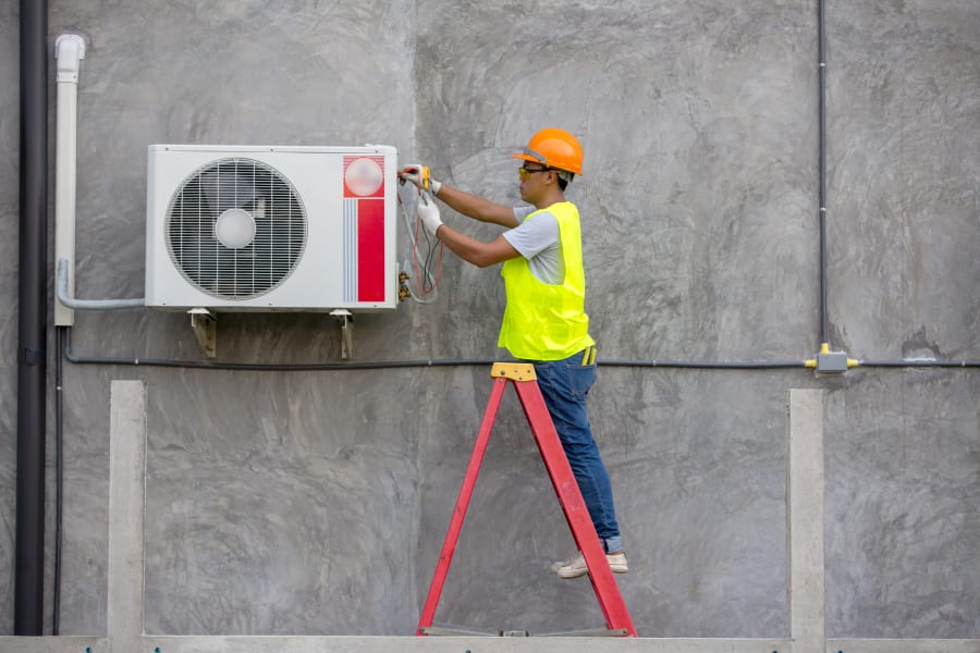 An air conditioner technician services an outdoor unit.