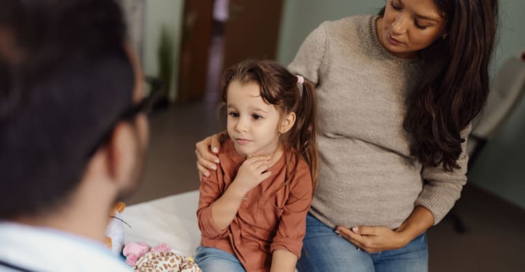 Small girl having a medical appointment with her pregnant mother at pediatricians'.