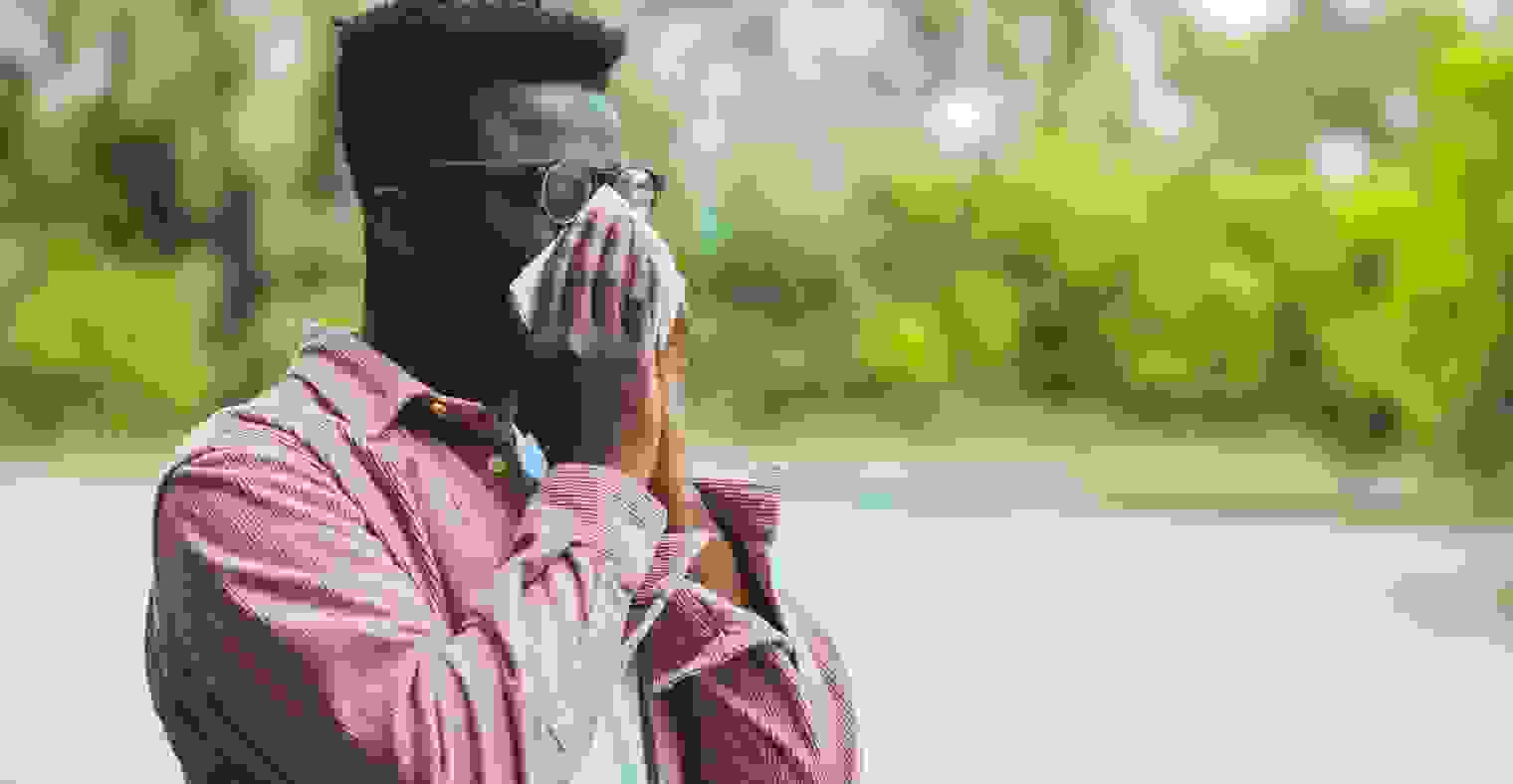 A Black man blowing his nose in a park