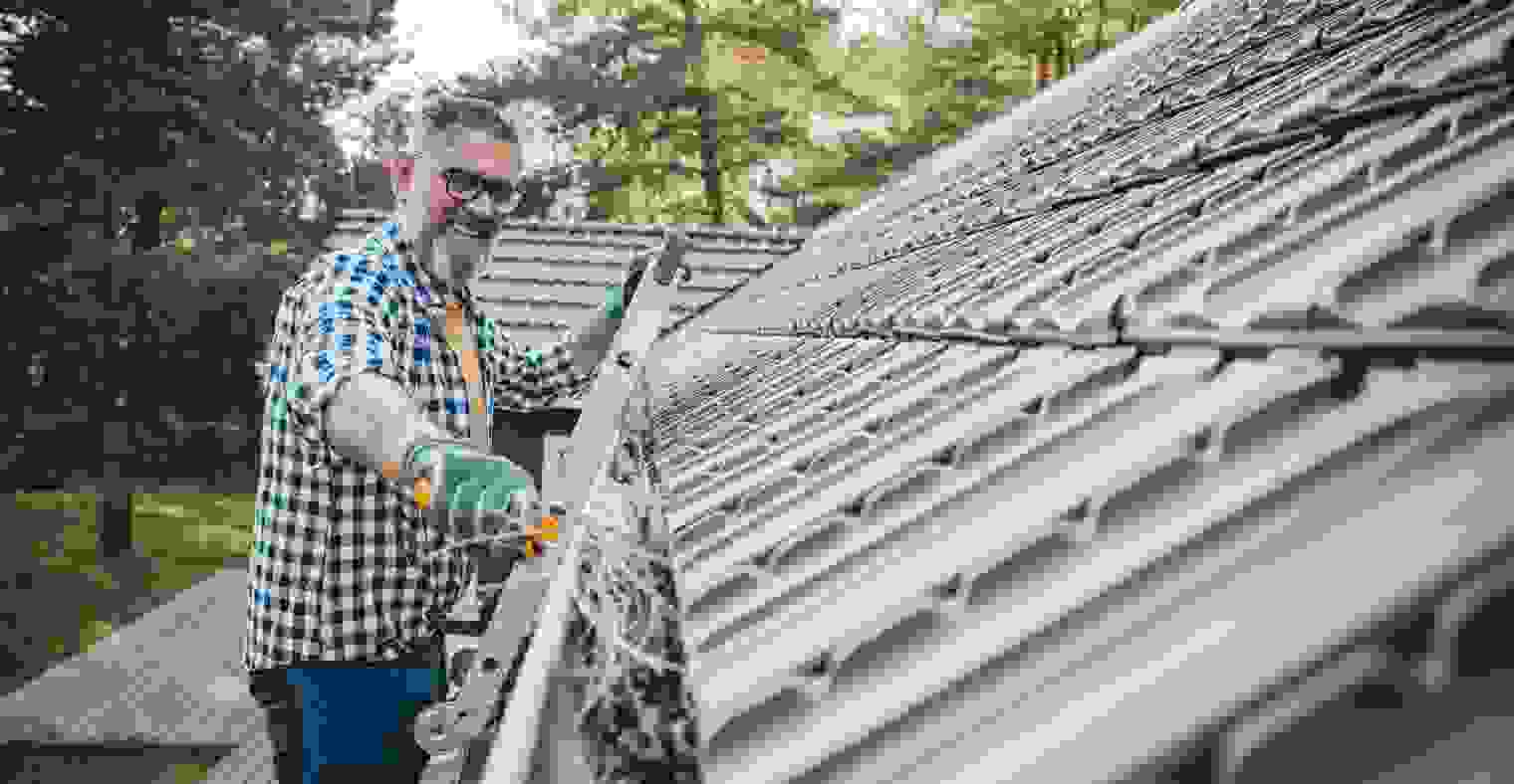 A man cleaning leaves from guttering of house