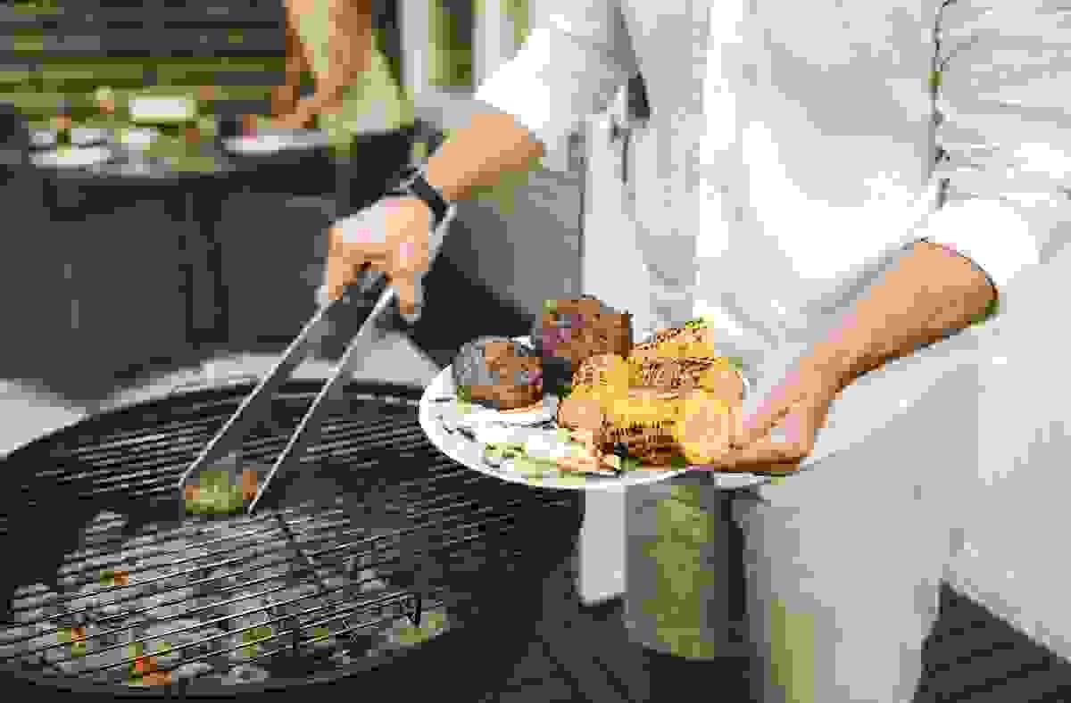 A man places grilled hamburgers on a plate.
