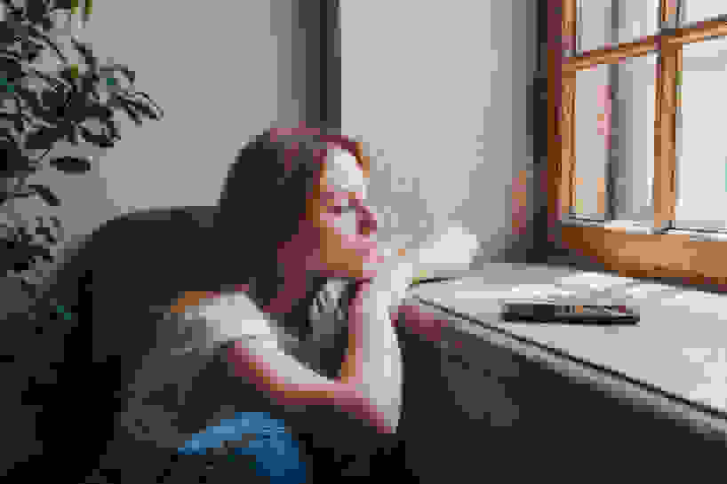 A woman sits forlornly at a window.