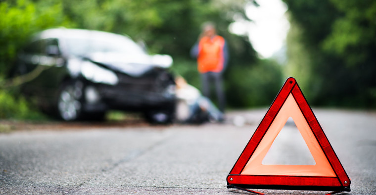 A close up of a red emergency triangle on the road in front of a car after an accident.