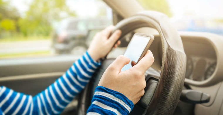 Woman driving car and texting message on smartphone