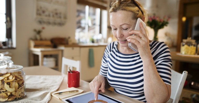 Senior woman at home working on tablet, making phone call