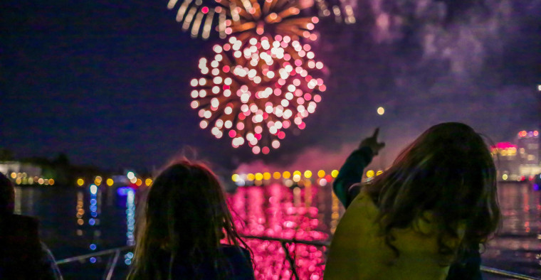 Kids in life jackets watch fireworks over the water.