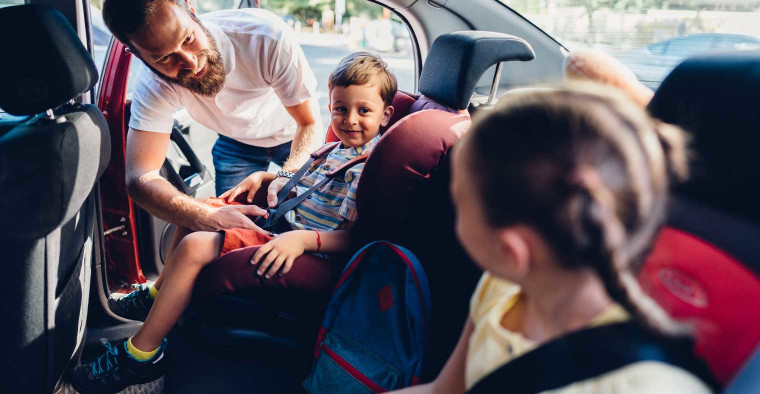 A father puts his kids into car seats.
