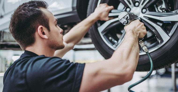 A mechanic affixing tires to a car.