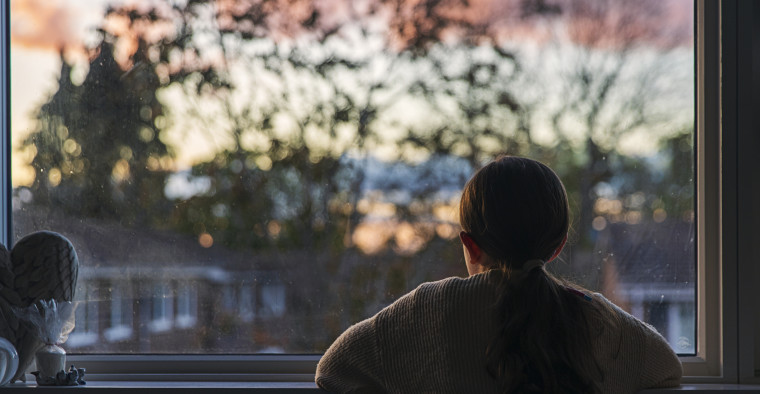 A young girl looks out of her window at sunset.