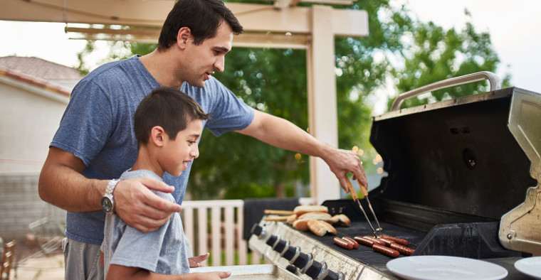 A father shows his son how to grill hot dogs.