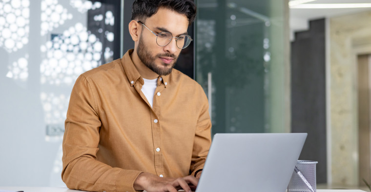 A young man in glasses working on a laptop in a stylish office setting