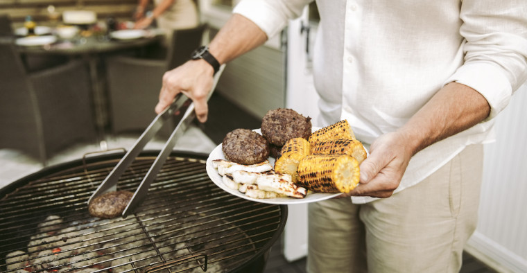 A man places grilled hamburgers on a plate.