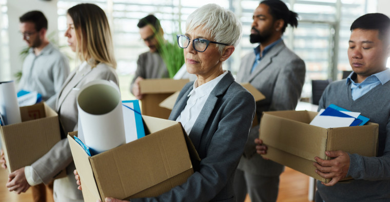 Large group of displeased business people carrying carton boxed with their belongings after being fired from their jobs.