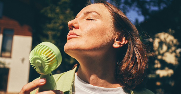 A woman beats the heat with a handheld fan.