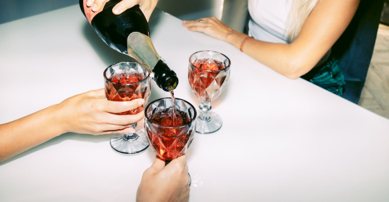 A person pours sparkling wine into friends' cups.