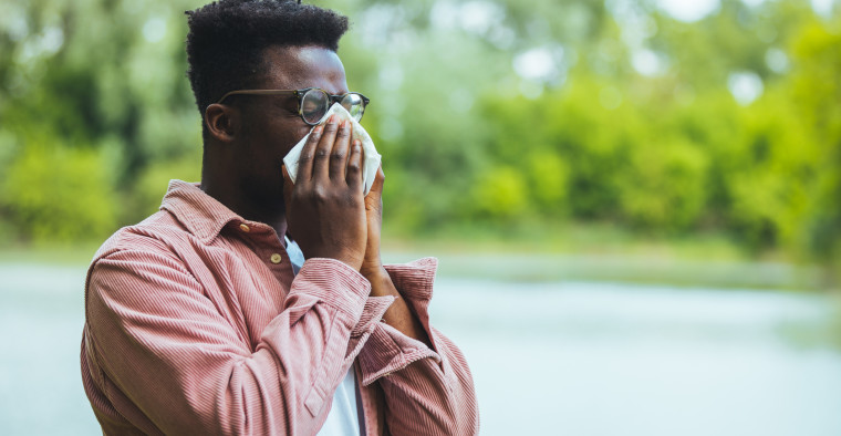 A Black man blowing his nose in a park