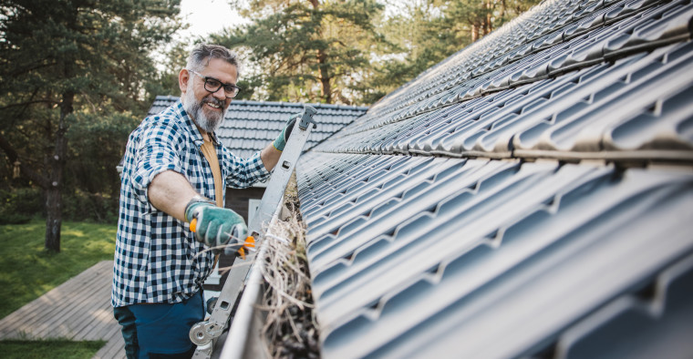 A man cleaning leaves from guttering of house