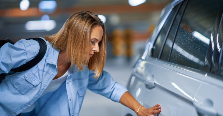 A woman examines car damage.