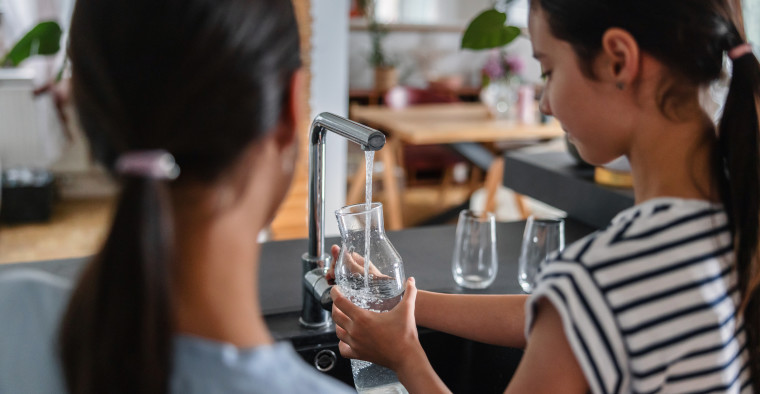 Two young sisters standing in front the sink filling up a glass jar with tap water