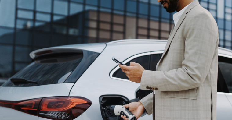 Man charging electric vehicle while looking at his phone