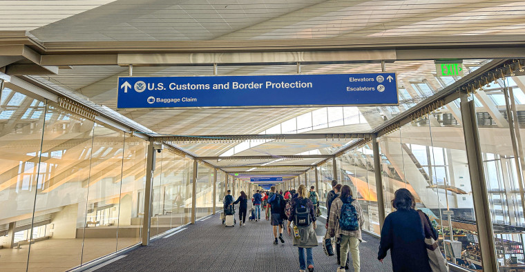 People in an airport walking under a U.S. Customs and Border Protection sign