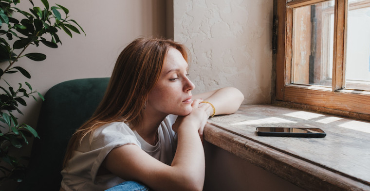 A woman sits forlornly at a window.