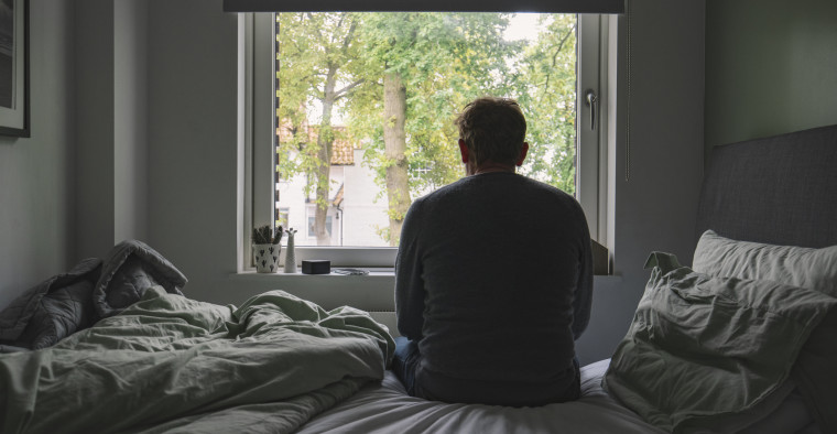 A man looks out his bedroom window.