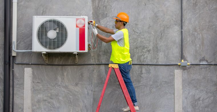 An air conditioner technician services an outdoor unit.