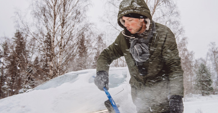 A man wipes snow from his car.