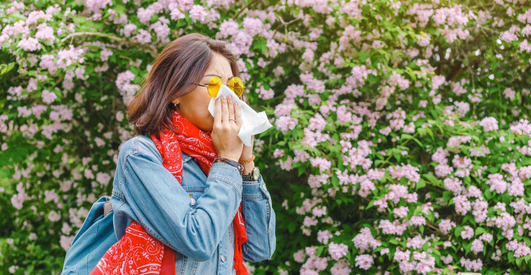 A woman sneezes near flowers.