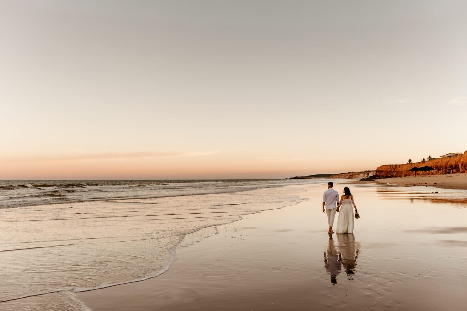 Couple walking on beach with a sunset woman wearing wedding dress