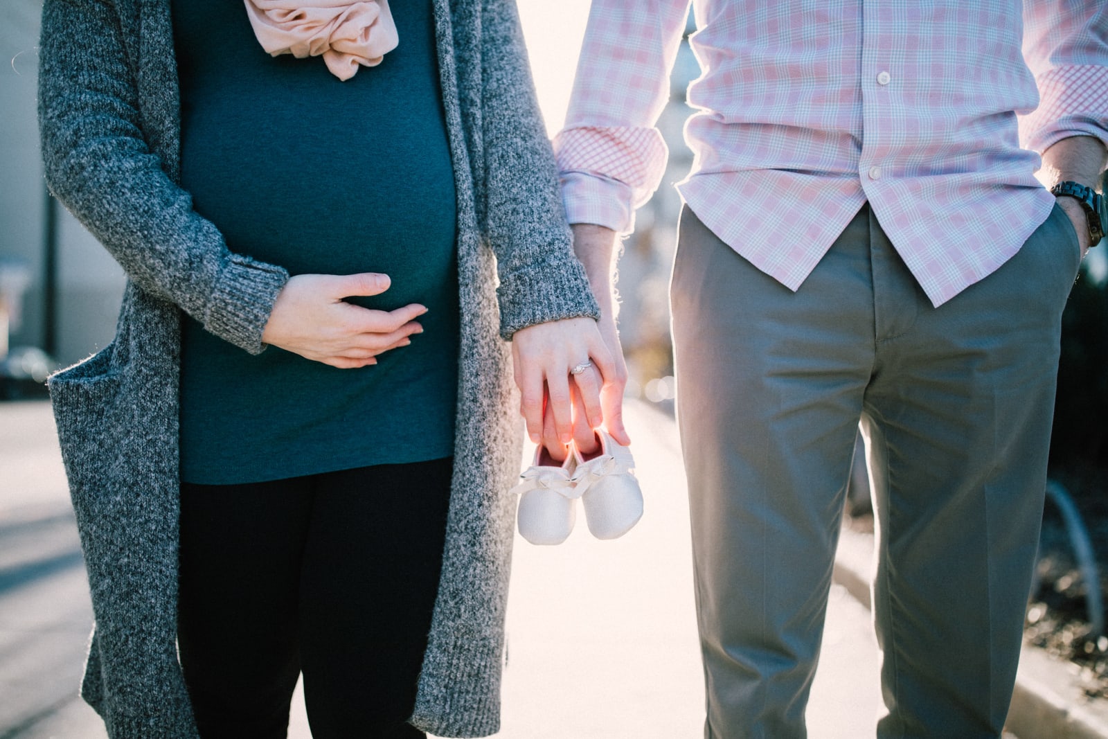 Couple comprising of a man and a pregnant woman holding hands with baby shoes on their hands