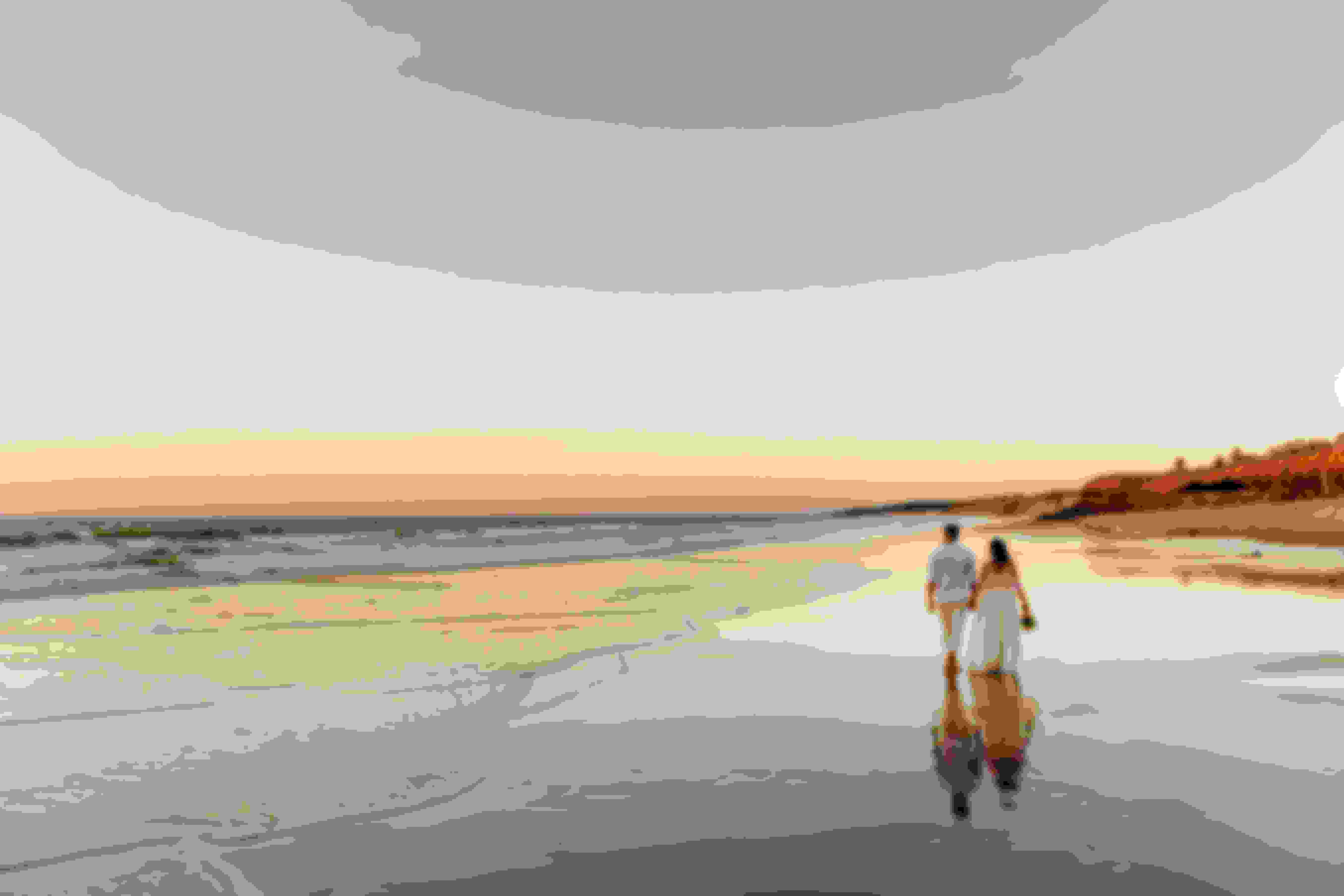 Couple walking on beach with a sunset woman wearing wedding dress