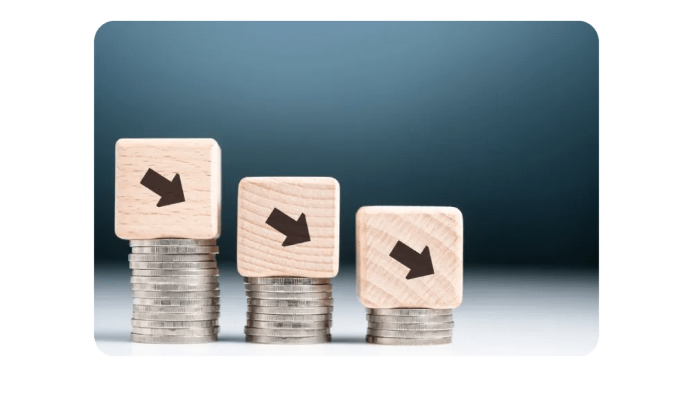 A visual representation of declining financial trends, with wooden blocks featuring downward arrows stacked on top of coins.