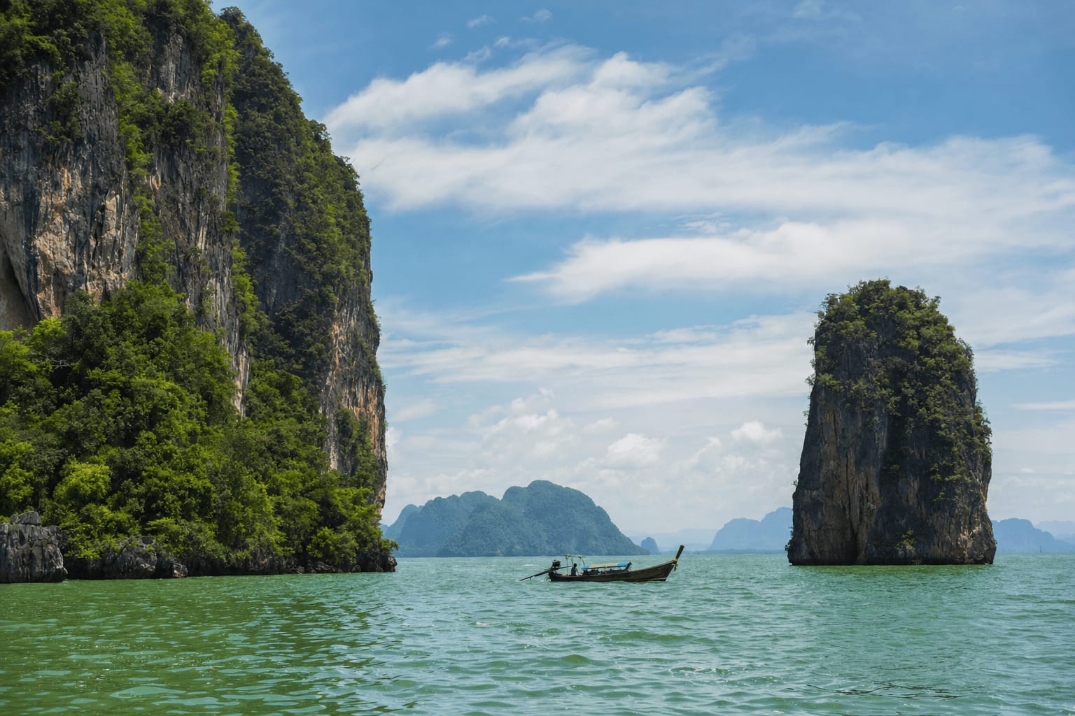 Veetrips Limestone cliffs rising from the water of Phang Nga Bay with a long-tail boat