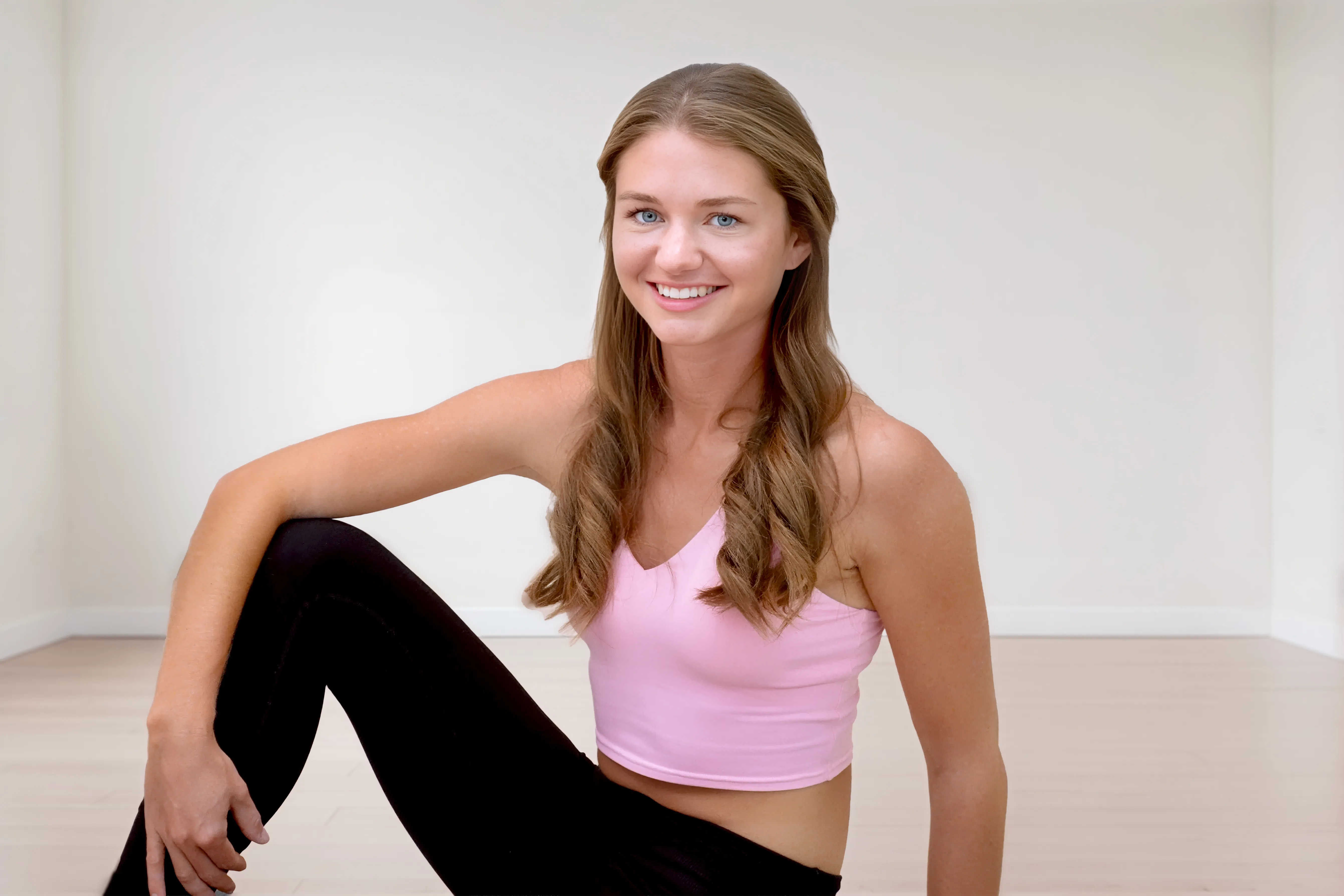 Junge Frau in Sportkleidung sitzt lächelnd auf dem Boden im Pilates Fit Kurs