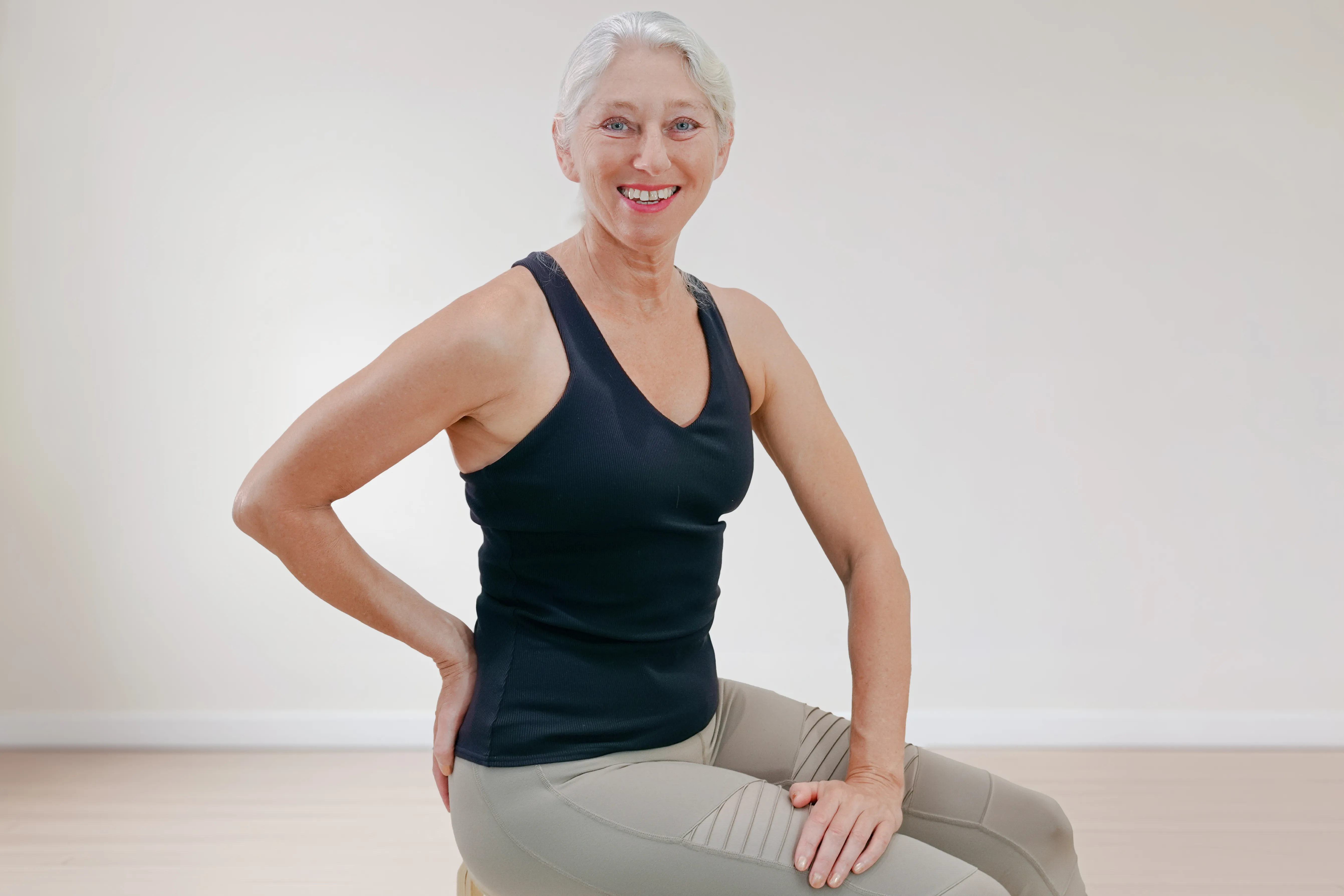 Ältere Frau sitzt aufrecht auf einem Hocker und lächelt im Pilates Light Kurs