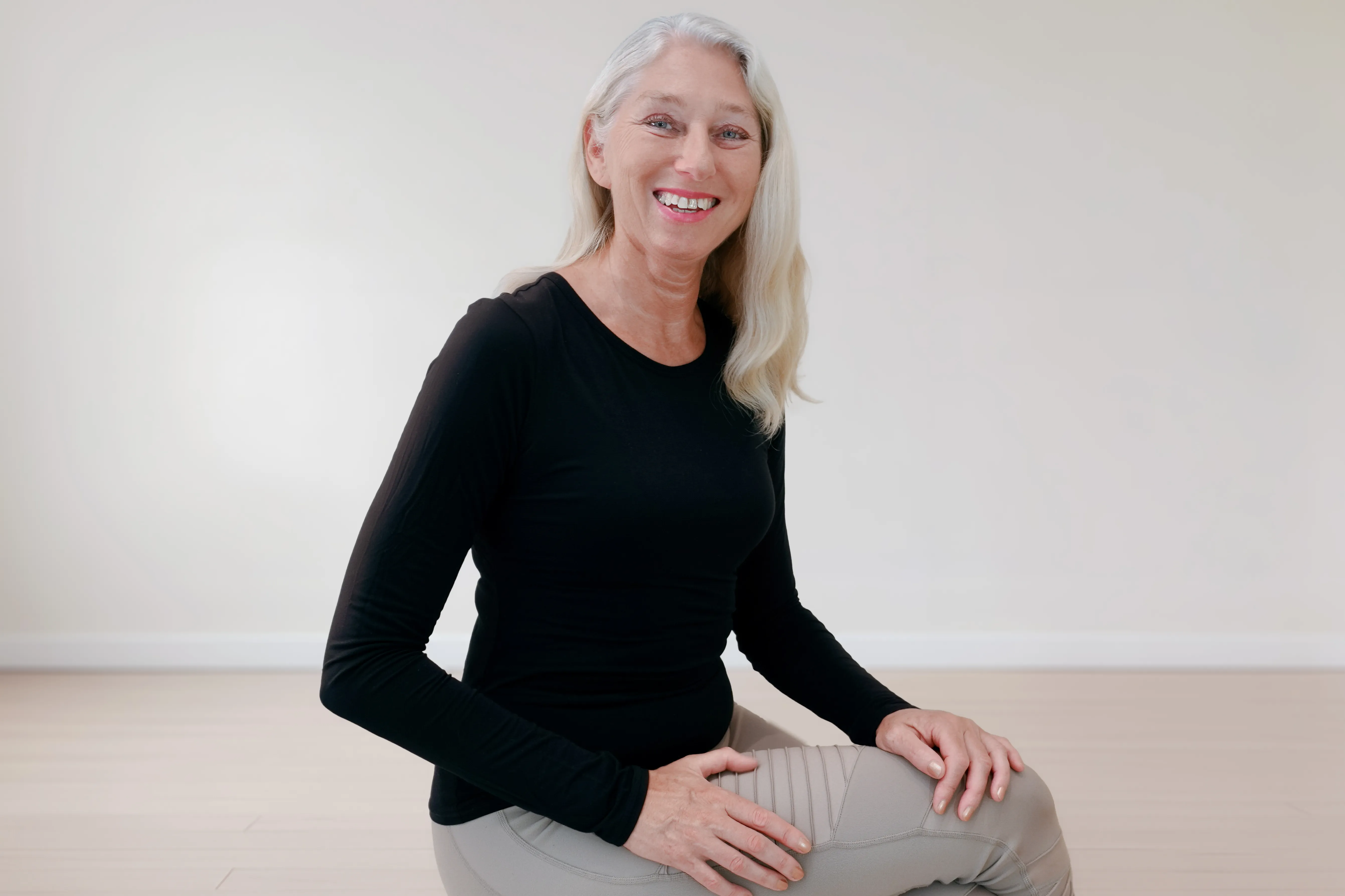 Pilates Trainerin sitzt lächelnd auf einem Hocker im Pilates Senior Kurs