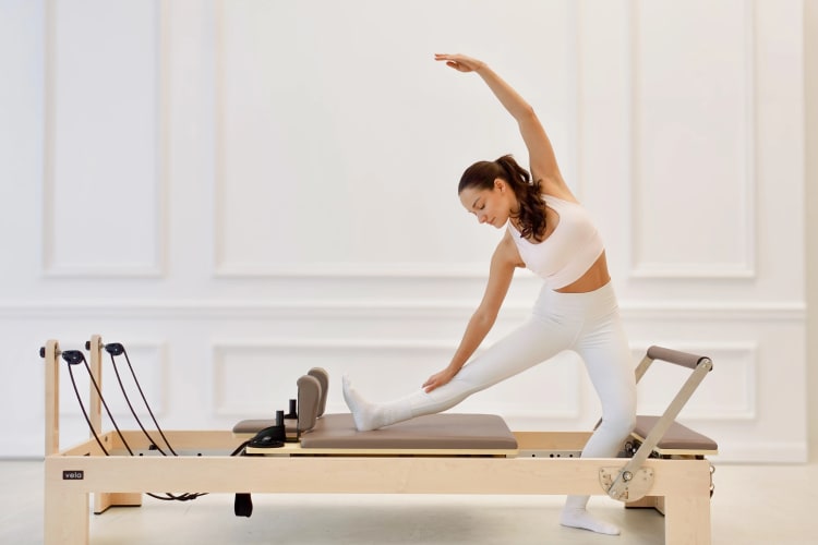 Eine Trainerin macht einen Spagat auf dem Reformer.
