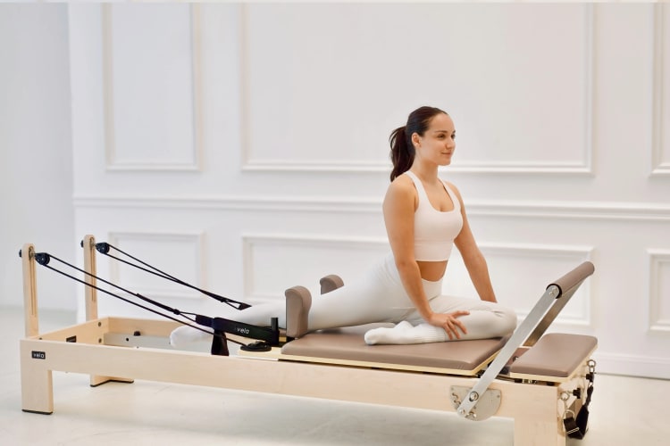 Eine Trainerin macht eine Dehnübung auf dem Reformer.
