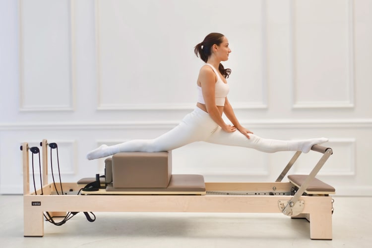 Eine Trainerin macht eine Dehnübung auf dem Reformer.