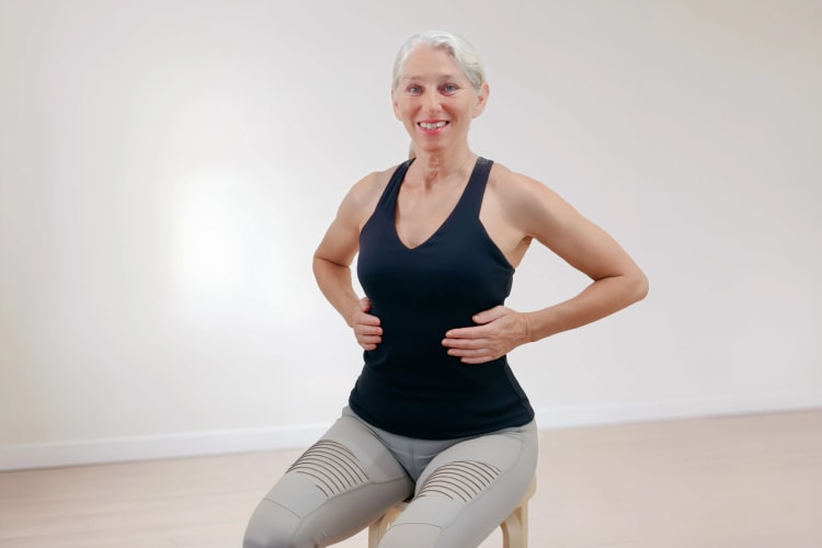 Eine Frau trainiert die Pilates Atmung im Sitzen