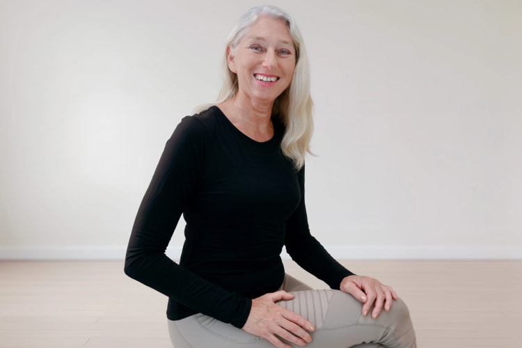 Pilates Trainerin sitzt lächelnd auf einem Hocker im Pilates Senior Kurs