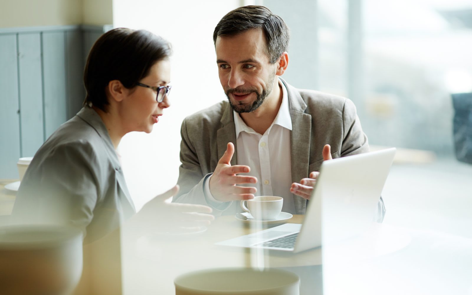 Two colleagues discussing hiring decisions over coffee with a laptop at the table